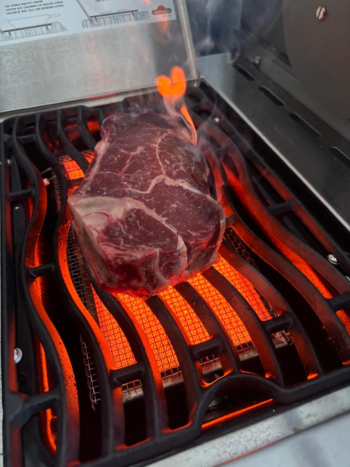 Rohes Rindersteak auf heißem Grillrost über glühender Kohle, BBQ Zubereitung für saftiges Steak mit intensiven Röstaromen