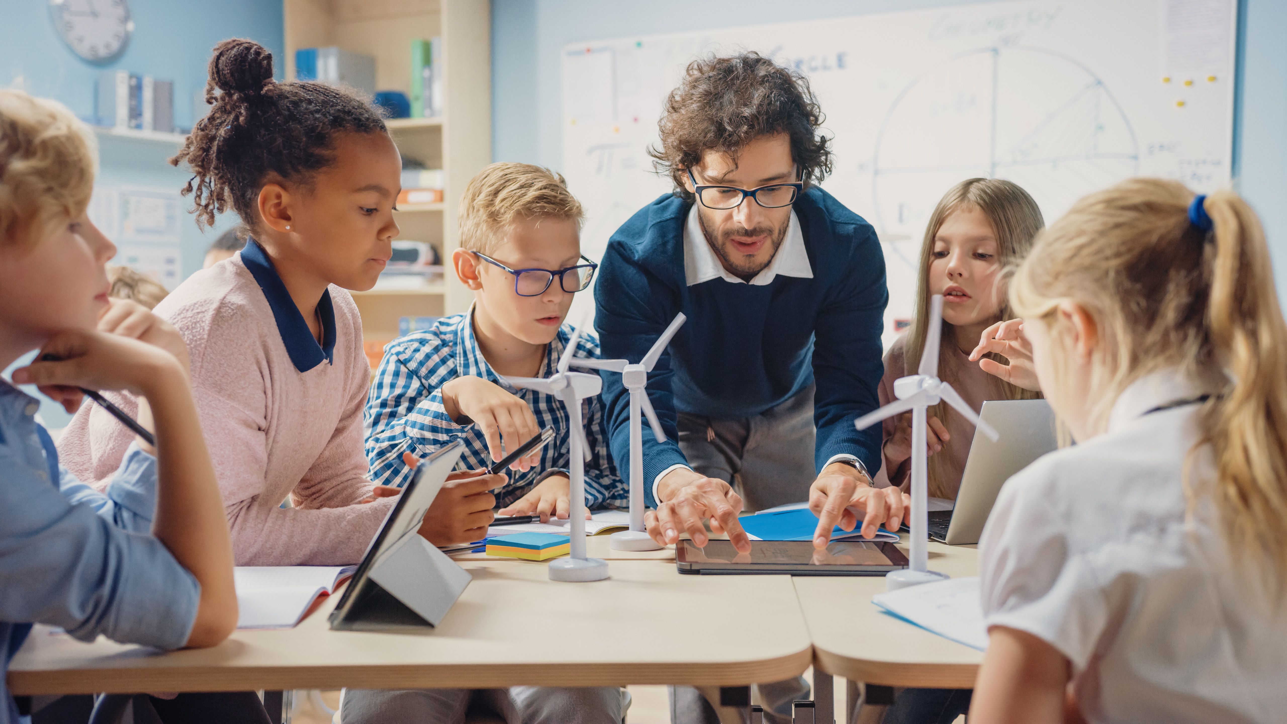 Lehrkraft und Kinder arbeiten gemeinsam an Medienprojekt im Unterricht, Einsatz digitaler und kreativer Methoden zur Förderung von Medienkompetenz und Teamarbeit