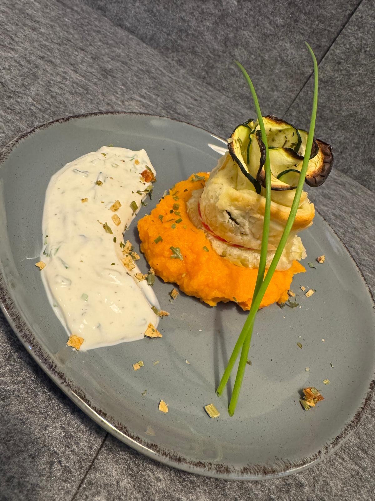 Vegetarisches Grillgericht mit gegrilltem Ziegenkäse auf Süßkartoffelpüree, Zucchini und cremiger Kräutersauce, kreativ angerichtet auf grauem Teller