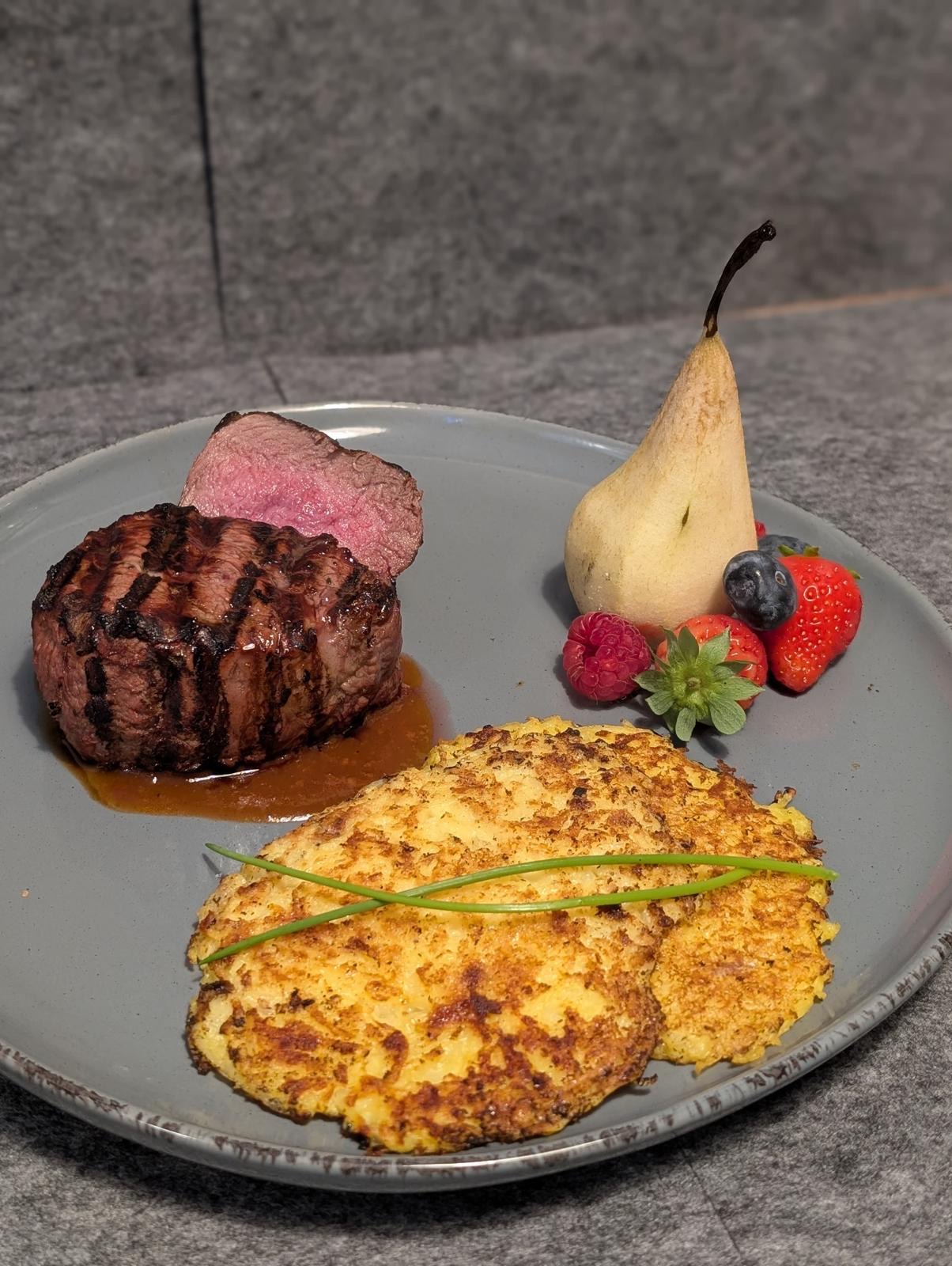 Saftiges Rindersteak mit Grillstreifen, Beilage aus Kartoffelgratin und frischen Früchten auf grauem Teller, Gourmetgericht in der gehobenen Küche