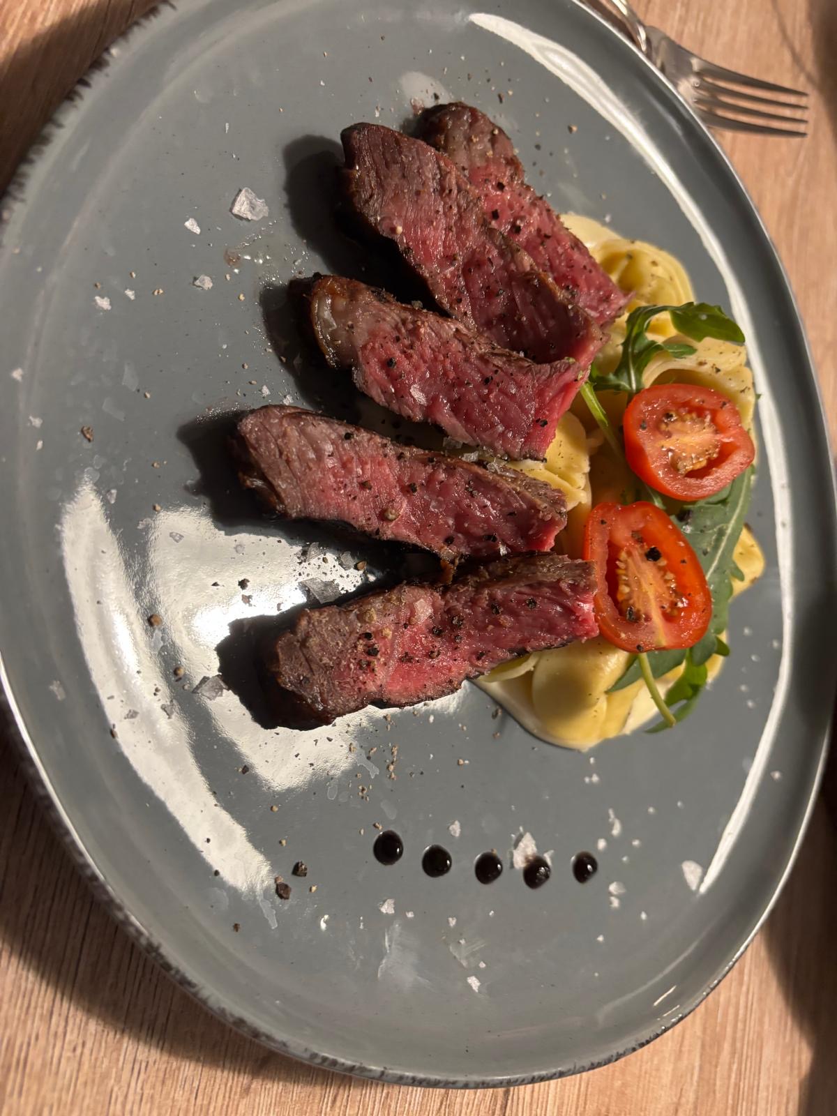 Medium rare Rindersteak in Scheiben geschnitten, serviert mit Kartoffelbeilage und frischen Tomaten auf modernem Teller, gehobene Küche Gericht